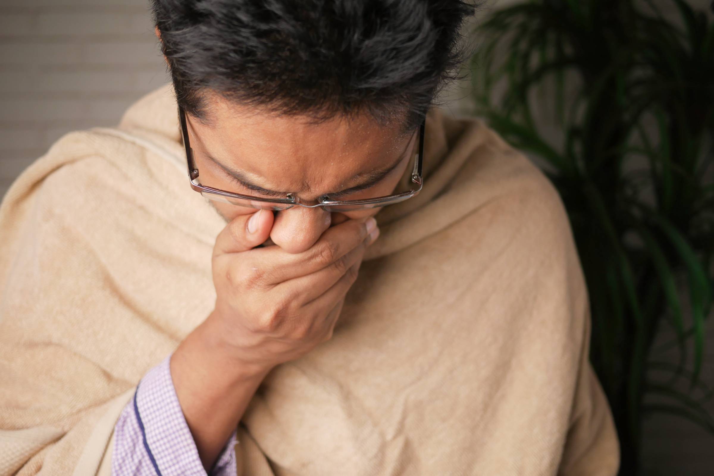 Person covering their mouth with hand, head lowered